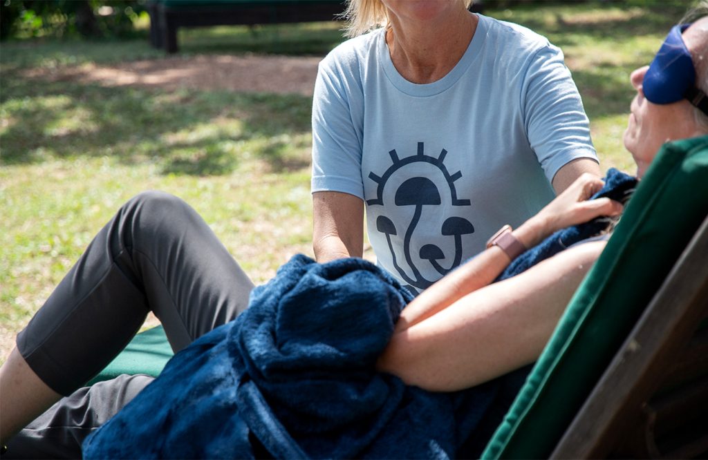 woman with eye-shades and covered with a blanket undergoing psilocybin therapy with a therapy alongside her