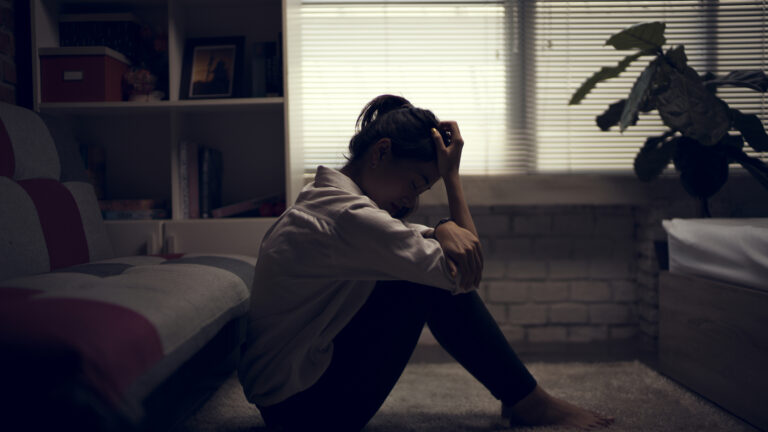 woman with depression sitting on the floor of a dark room