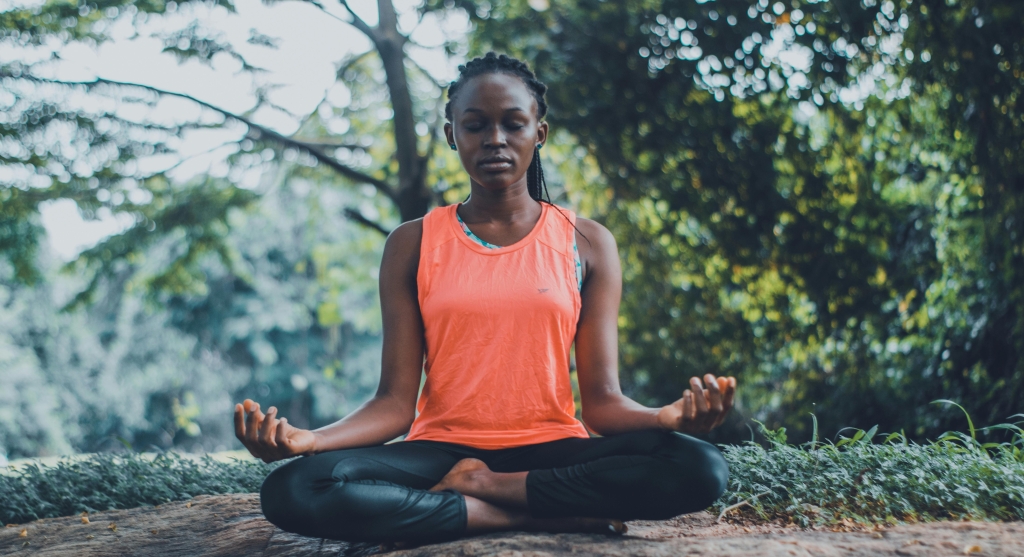 Woman sitting on a flat rock within a forest meditating
