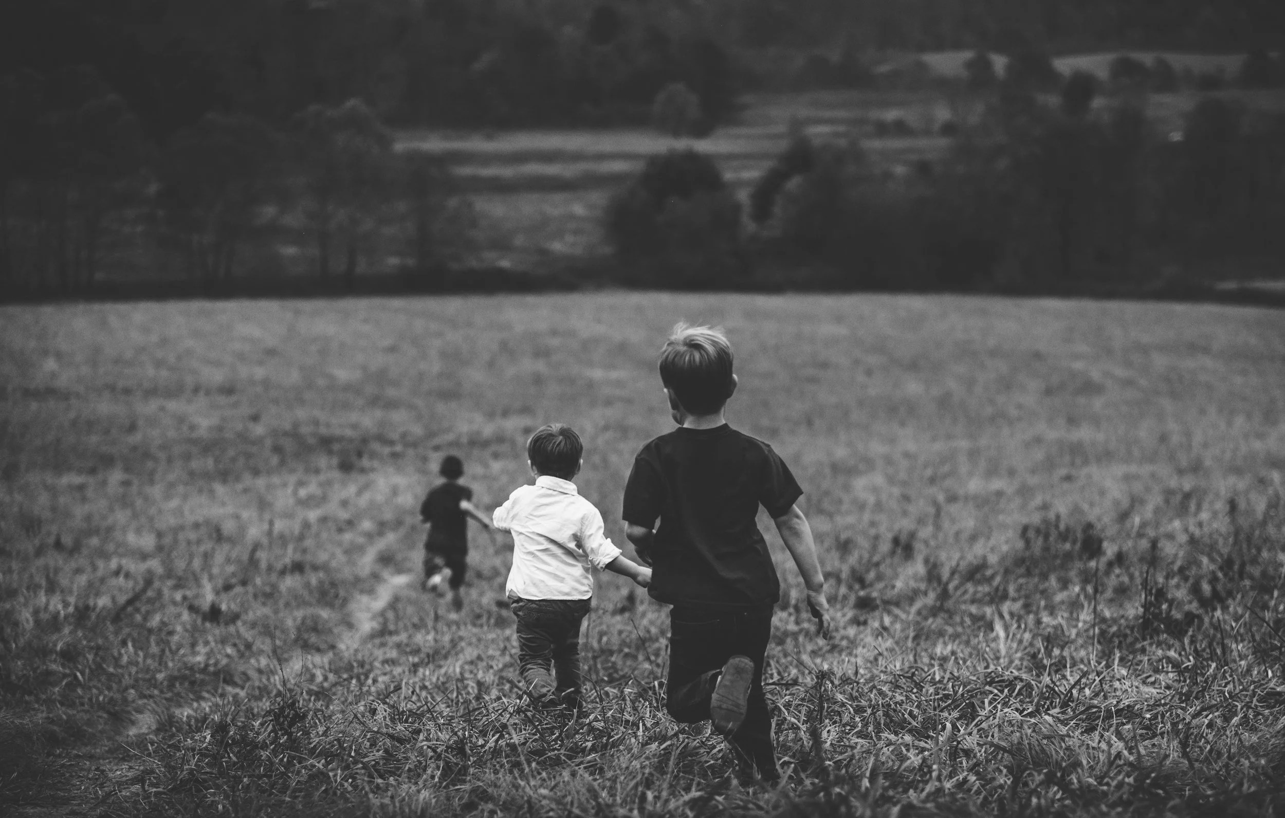 Black and white image of three children running free through a field.