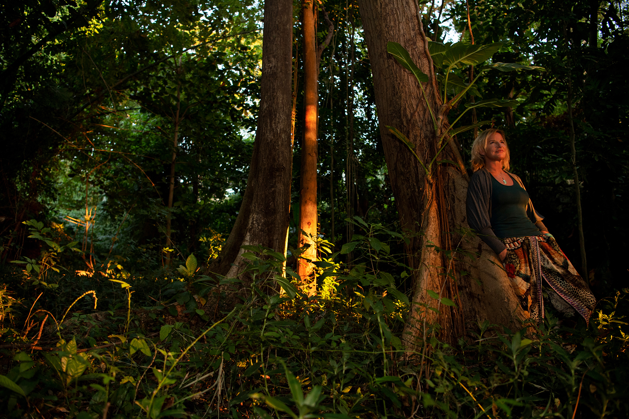 A woman leaning back on a large tree in a jungle setting at MycoMeditations psychedelic retreat.