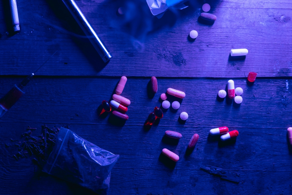 Ominous photo of pills and illicit drugs on a wooden table.