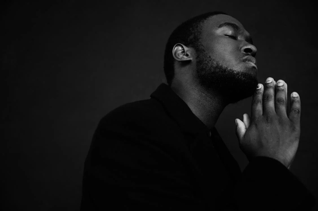 black and white photo of man praying on solid black background.
