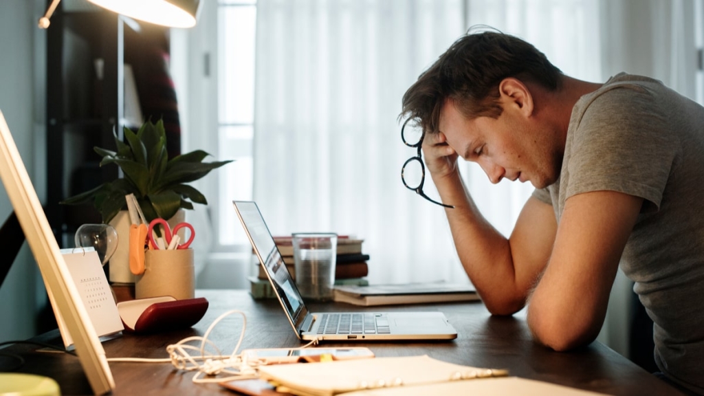 Guy sitting at desk with hand on forehead exhausted with burnout.