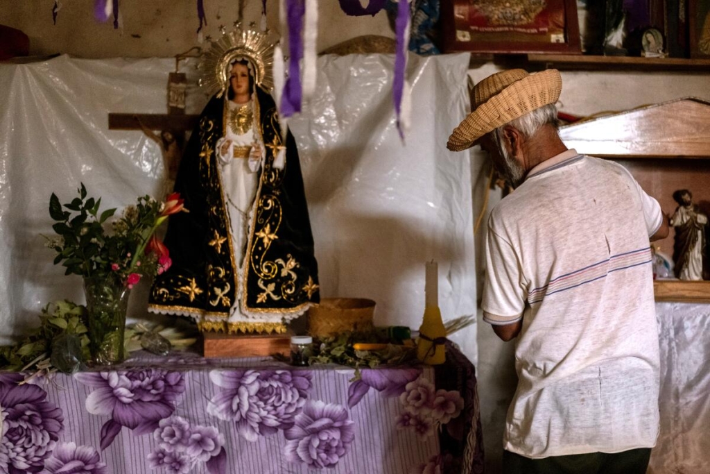 A man prepares a mushroom ceremony by an alter with Catholic symbols, including Mary.